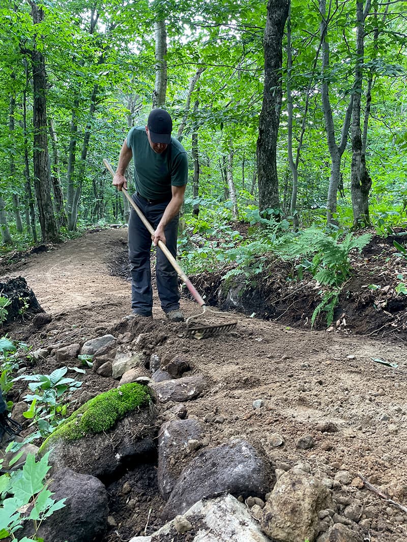 Employé de Mont Bélair Découvertes qui râtelle un sentier.